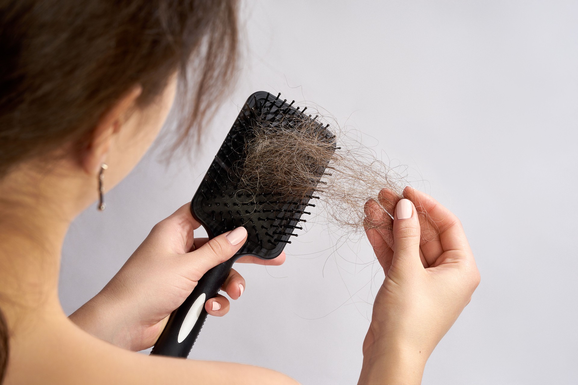 Woman holding a brush with hair shed due to alopecia, thinking about booking a free consultation with a specialist at Bespoke Aura